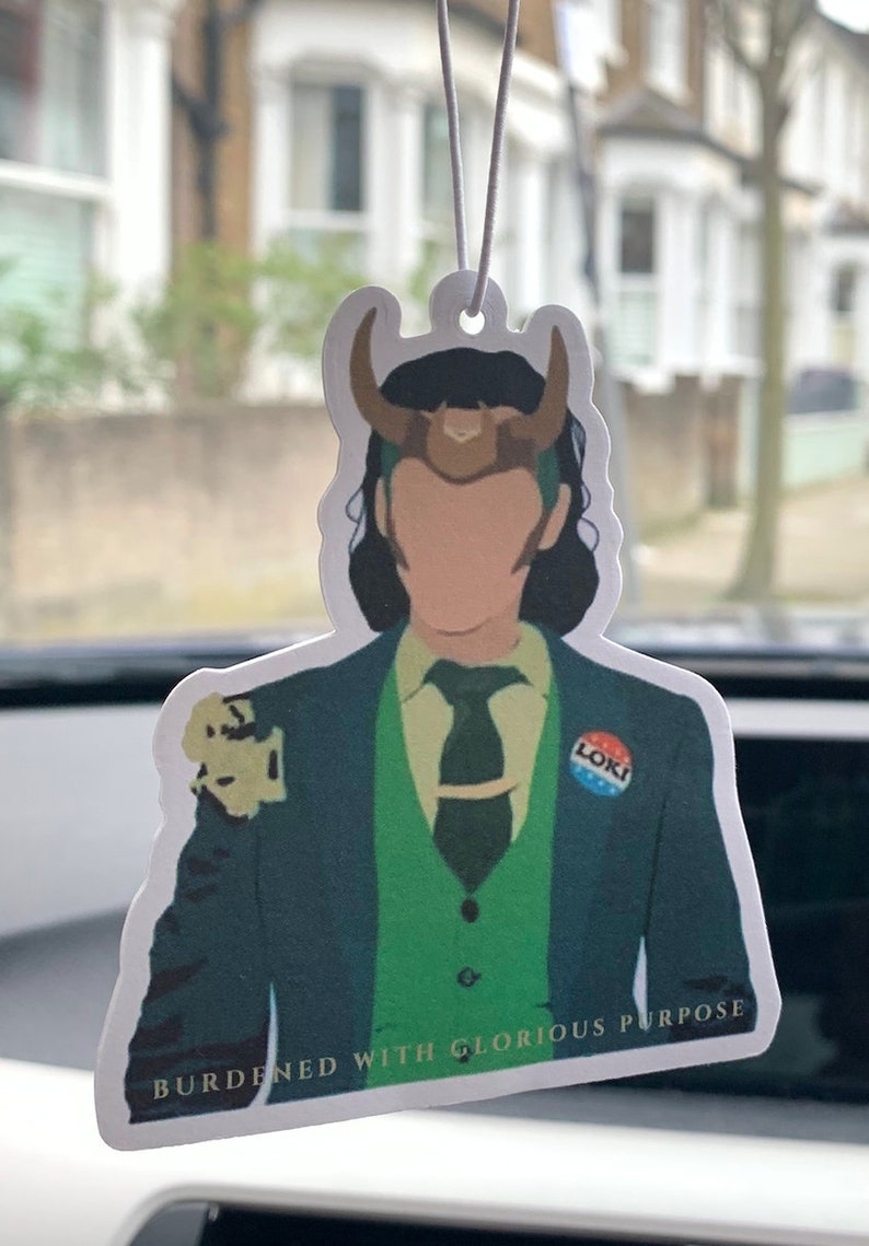 May include: A white car air freshener featuring a cartoon illustration of Loki from the Marvel Cinematic Universe. He is wearing a green suit, a green vest, and a brown horned helmet. The text "Burdened with Glorious Purpose" is printed at the bottom of the air freshener.