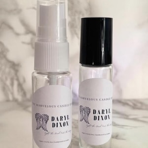 May include: Two clear glass bottles with white labels. The labels have a black and white graphic of angel wings and the text "Daryl Dixon" with the tagline "Let the good times roll".