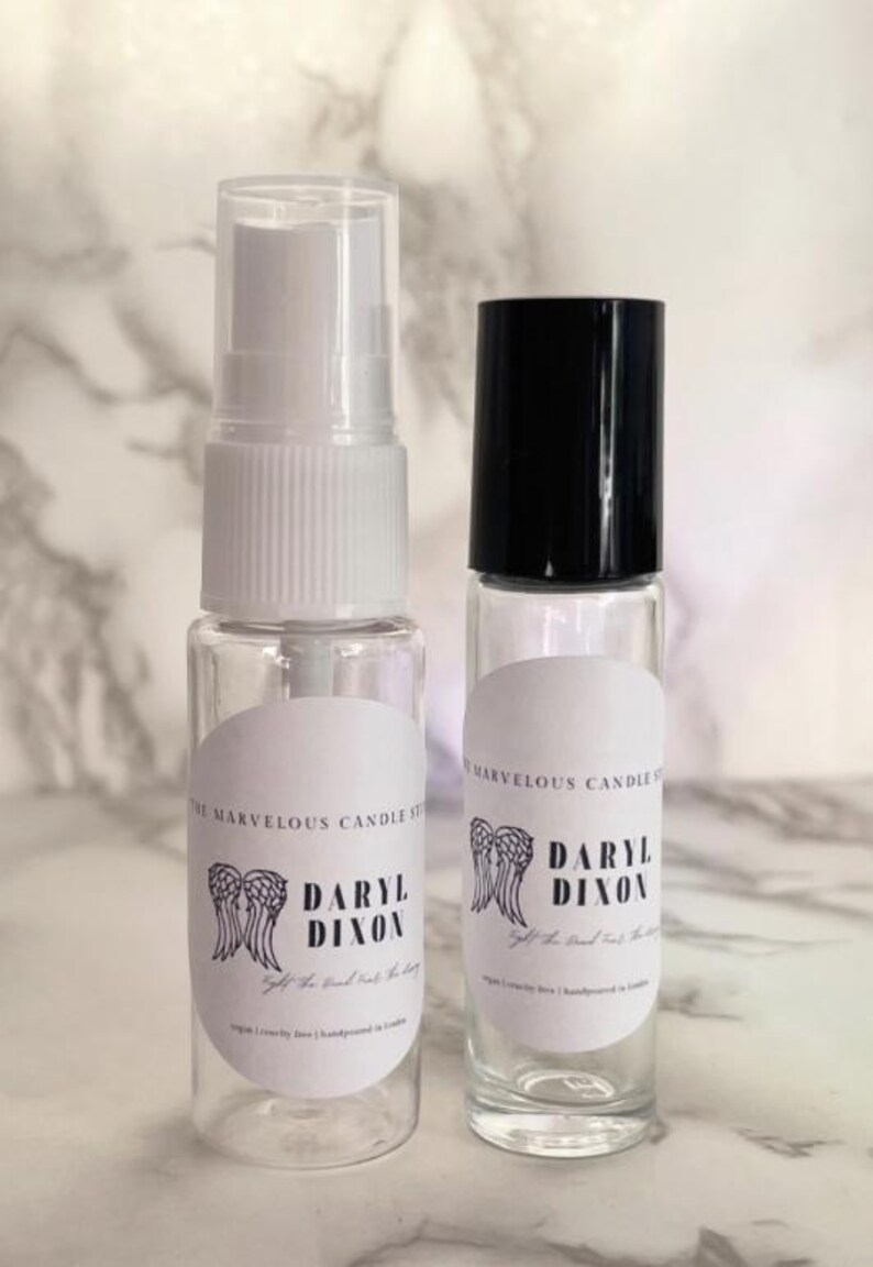 May include: Two clear glass bottles with white labels. The labels have a black and white graphic of angel wings and the text "Daryl Dixon" with the tagline "Let the good times roll".