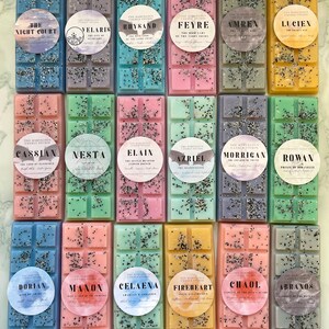 May include: A collection of colorful wax melt bars in various shades, including blue, pink, green, and yellow. Each bar is decorated with glitter and a circular label with a name. The bars are arranged in rows, showcasing a variety of scents.