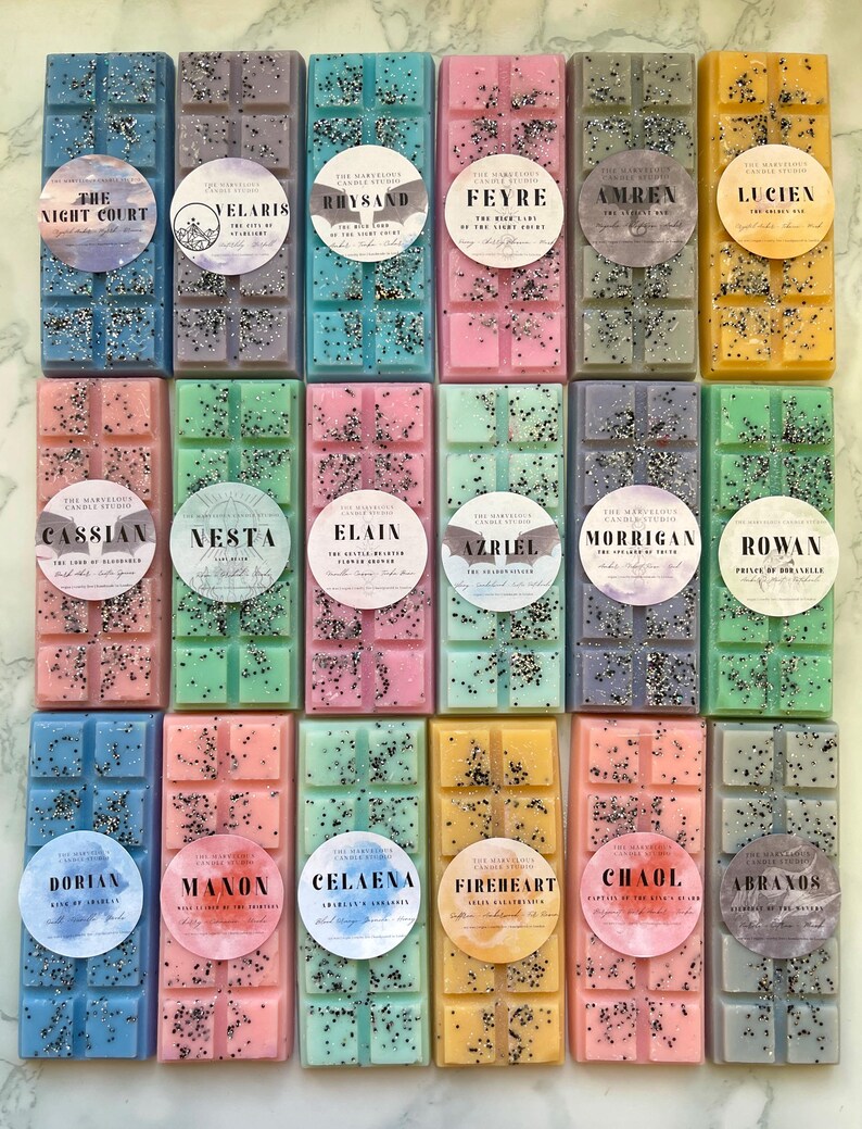 May include: A collection of colorful wax melt bars in various shades, including blue, pink, green, and yellow. Each bar is decorated with glitter and a circular label with a name. The bars are arranged in rows, showcasing a variety of scents.
