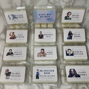 May include: Twelve white square candle containers with clear plastic lids. Each container has a different celebrity's photo and name printed on the front. The text "The Marvelous Candle Studio" is printed at the top of each container.