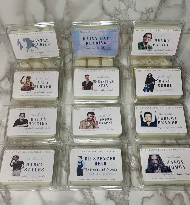 May include: Twelve white square candle containers with clear plastic lids. Each container has a different celebrity's photo and name printed on the front. The text "The Marvelous Candle Studio" is printed at the top of each container.