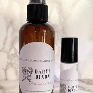 May include: Two brown glass bottles with white labels. The larger bottle is a spray bottle and the smaller bottle is a roll-on bottle. Both bottles have a black and white graphic of angel wings and the text "Daryl Dixon" with the tagline "Fight the good fight, for the living".