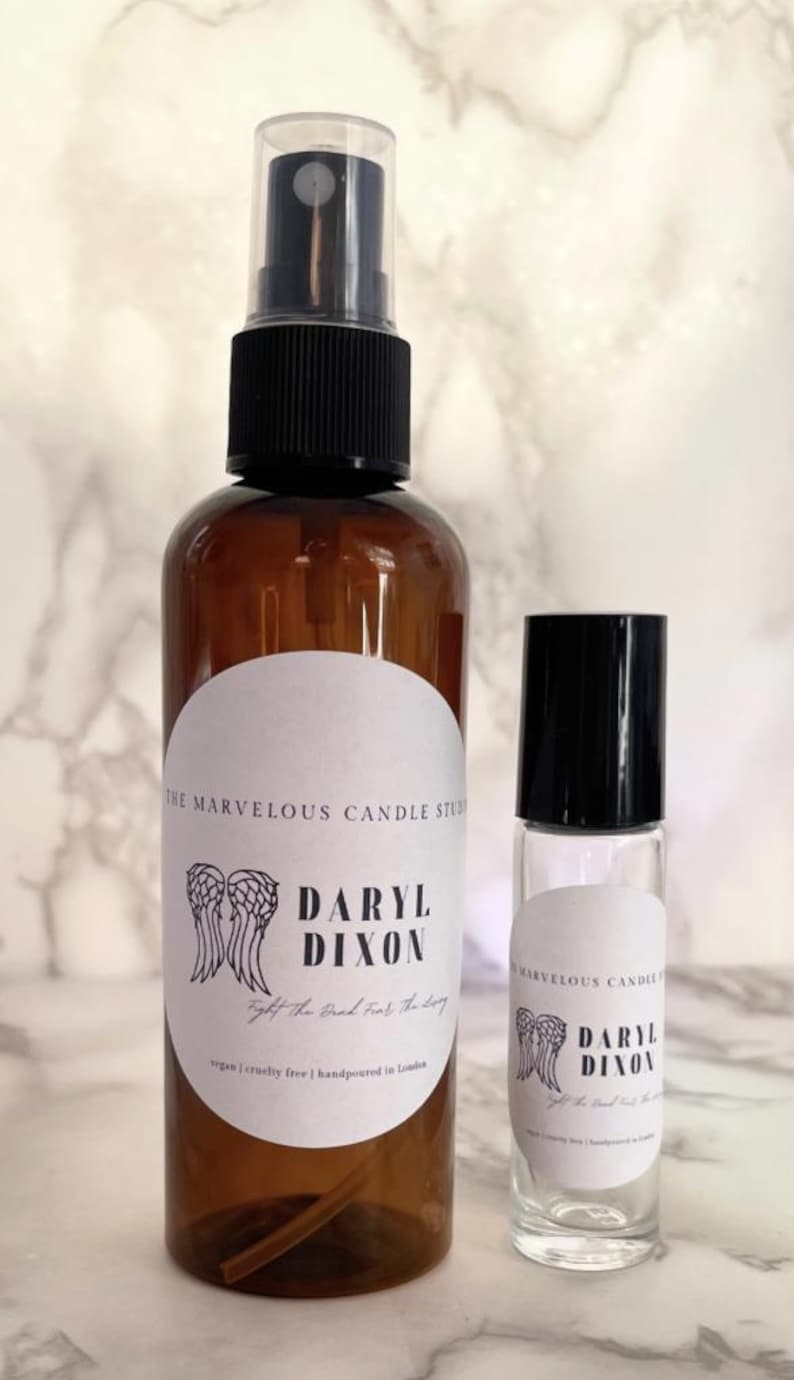 May include: Two brown glass bottles with white labels. The larger bottle is a spray bottle and the smaller bottle is a roll-on bottle. Both bottles have a black and white graphic of angel wings and the text "Daryl Dixon" with the tagline "Fight the good fight, for the living".