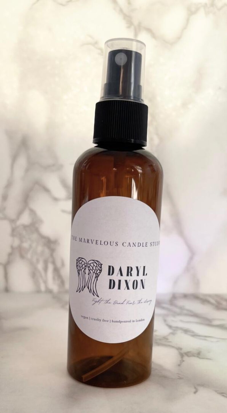 May include: A brown glass bottle with a black spray top and a white label. The label has a black and white illustration of angel wings and the text "Daryl Dixon" and "The Good, The Bad, The Ugly".