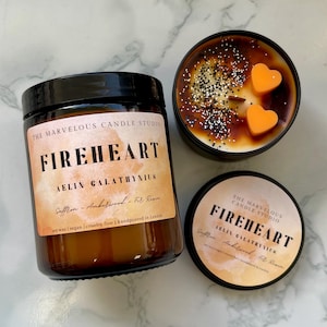 May include: Three candles from The Marvelous Candle Studio. One is in a glass jar with a black lid, labelled "FIREHEART". Another is in a black tin with orange heart-shaped wax melts. The third is a small tin with the same label.
