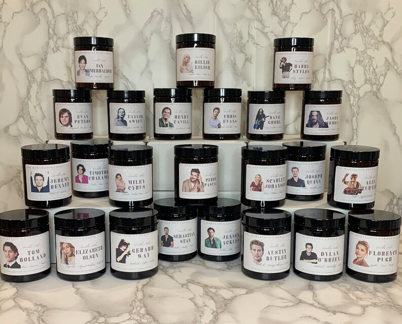 May include: A collection of 30 brown glass candle jars with black lids. Each jar features a different celebrity's face on the label. The candles are arranged in three rows of ten.