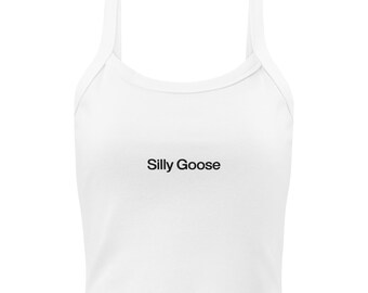 Puede incluir: Top corto blanco con tirantes finos y el texto "Silly Goose" en negro. El top tiene un escote redondo y una silueta ajustada. La tela parece ser un material suave y acanalado.