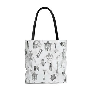 May include: White tote bag with a black handle and a pattern of anatomical illustrations on a marble background. The illustrations include a skull, bones, a rib cage, a spine, a heart, lungs, and a brain.