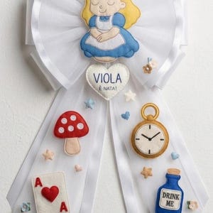 Può includere: Una decorazione da parete in nastro bianco con un personaggio in feltro dai capelli biondi e vestito blu, un cuore in feltro con la scritta VIOLA È NATA!, un fungo rosso, un orologio da taschino dorato, un asso di cuori e una bottiglia blu DRINK ME.
