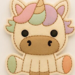 Può includere: Un'applicazione in feltro a forma di unicorno con corpo color crema, muso beige e un corno centrale. La criniera è composta da sezioni rosa pastello, verde menta e lavanda. L'unicorno presenta occhi neri circolari e cuciture a vista.