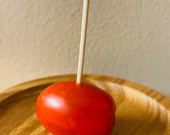 May include: A red tomato on a wooden plate with a white pearl on a wooden skewer.