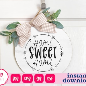 May include: A white round wooden sign with the text "Home Sweet Home" in black script lettering. The sign is decorated with a black arrow design and a brown and white gingham ribbon.