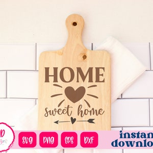 Può includere: Un tagliere di legno con il testo "HOME sweet home" e un design a forma di cuore. Il tagliere è su uno sfondo di piastrelle bianche.