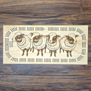 May include: A wooden game board with a sheep theme. The board has a circular track with holes for marbles and a start and finish line. The board is decorated with four sheep illustrations.