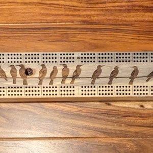 May include: A wooden cribbage board with a line of birds carved into the surface. The board has a dark brown stain and is made of wood.