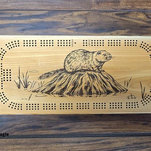 May include: A wooden cribbage board with a black and white illustration of a beaver sitting on a log. The board has a traditional cribbage board design with holes for pegs and a scoring track.