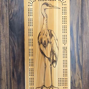 Peut inclure: Un plateau de jeu de cribbage en bois avec un motif de héron bleu gravé au laser. Le plateau est en bois brun clair avec une bordure brun foncé. Le plateau mesure 45,7 cm de haut et 15,2 cm de large.