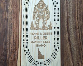 May include: A personalised wooden cribbage board featuring a Bigfoot illustration, the text "FRANK & JENNIE PILLER HAYDEN LAKE, IDAHO" and an outline of the state of Idaho.