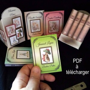 Może przedstawiać: Zestaw pięciu miniaturowych książek z ilustracjami postaci Beatrix Potter. Książki są zatytułowane "Beatrix Potter", "Noisette l'écureuil", "Sophie Cantang", "Jeannot Lapin" i "Pierre Lapin". Książki są wyświetlane na białym tle z tekstem "PDF à télécharger" w kolorze czarnym.