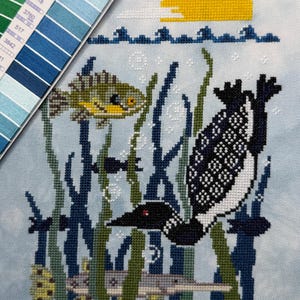 Könnte beinhalten: Kreuzstichmuster mit einer Eistaucher, Fischen und Wasserpflanzen in einer Unterwasserszene. Der Eistaucher ist schwarz und weiß, die Fische sind grün und gelb, und die Sonne ist gelb. Eine Farbpalette befindet sich in der oberen linken Ecke.