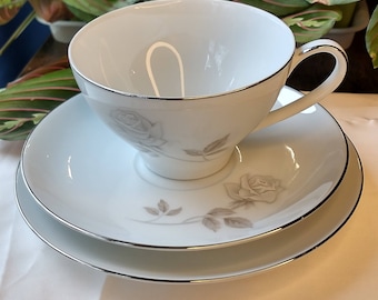 May include: A white teacup and saucer set with a silver trim and a delicate gray rose design.