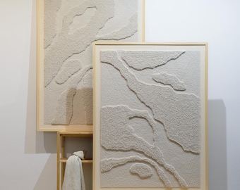 Puede incluir: Dos obras de arte murales abstractas enmarcadas. La obra presenta un diseño texturizado y en relieve en tonos beige y crema, enmarcados en marcos de madera clara. Las piezas se exhiben contra una pared blanca, creando una estética minimalista.