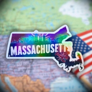 Könnte beinhalten: Ein holografischer Aufkleber in Form von Massachusetts, mit einer Skyline-Silhouette und dem Staatsnamen. Eine rote Hummer-Grafik ist enthalten. Der Aufkleber befindet sich auf einer Karte und einer amerikanischen Flagge.
