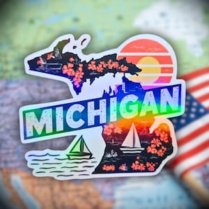 May include: A holographic sticker in the shape of the state of Michigan, featuring a sunset design and the word "MICHIGAN". The sticker includes illustrations of sailboats, flowers, and a lighthouse.