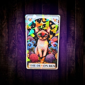 May include: A rectangular card featuring a holographic finish and an illustration of a Devon Rex cat centered among colorful flowers and stars. The text THE DEVON REX is printed in black capital letters at the bottom of the card design.