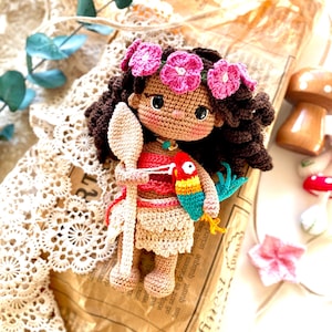 Puede incluir: Mu&ntilde;eca de ganchillo hecha a mano con cabello rizado casta&ntilde;o oscuro, una corona de flores rosas y una parte superior roja. La mu&ntilde;eca sostiene una cuchara de madera y un loro colorido. La mu&ntilde;eca lleva una falda beige y un collar turquesa.