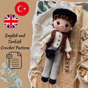 May include: A crocheted doll dressed in a white shirt, brown vest, and gray pants, with a black hat and bag. The doll has rosy cheeks and brown hair. The image includes the text "English and Turkish Crochet Pattern" and a PDF icon.