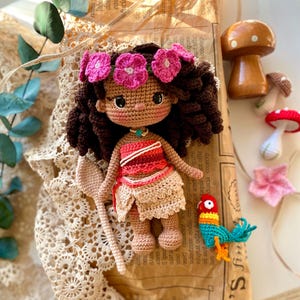 Puede incluir: Mu&ntilde;eca de ganchillo hecha a mano con cabello casta&ntilde;o, una corona de flores rosas y una parte superior roja y blanca. La mu&ntilde;eca sostiene una cuchara de ganchillo y est&aacute; acompa&ntilde;ada de un loro de ganchillo y decoraciones de hongos.
