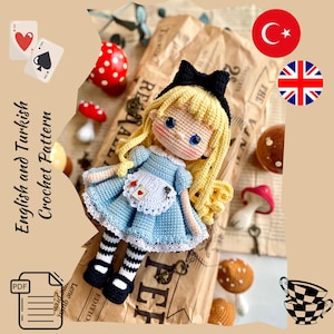 Può includere: Bambola all'uncinetto ispirata ad Alice nel Paese delle Meraviglie, con un vestito blu chiaro, un fiocco nero e capelli biondi. La bambola è circondata da funghi decorativi e carte da gioco. Il testo "English and Turkish Crochet Pattern" è visibile.