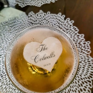Peut inclure: Un gla&ccedil;on en forme de c&oelig;ur avec le texte "The Colwells 08.18.23" en calligraphie noire, flottant dans un verre de champagne.