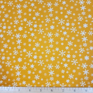 May include: A yellow fabric with a white snowflake pattern. The fabric is shown with a ruler for scale.