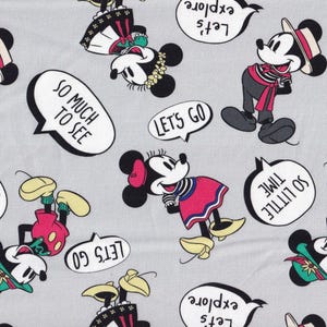 May include: Gray fabric featuring a repeating pattern of Mickey and Minnie Mouse characters in various outfits. Speech bubbles with phrases like "Let's Explore" and "So Much to See" are scattered throughout the design. The characters are in red, black, white, and yellow.