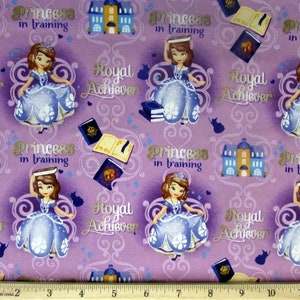 May include: Purple fabric with a repeating pattern of a cartoon princess in a blue dress, a castle, and books. The text "Princess in training" and "Royal Achiever" is repeated throughout the fabric.