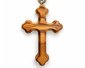 May include: A wooden cross pendant featuring a natural light brown grain pattern with dark brown streaks. The cross has rounded, flared ends and is suspended from a dark brown cord by a small, circular brass-colored metal jump ring connector.