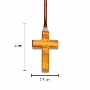 A wooden cross pendant, measuring 4 cm in height and 2.5 cm wide, hangs from a brown cord. The cross is crafted from light-toned wood with a visible grain, and a gold-coloured metal loop attaches it to the cord.