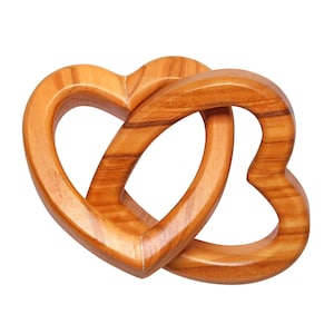 Puede incluir: Dos corazones de madera entrelazados, creando una sola forma de corazón. Los corazones son de color marrón claro con veta de madera visible.