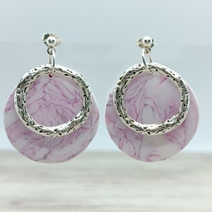 May include: A pair of silver and pink earrings with a marbled design. The earrings are round and have a silver ring around the outside.