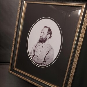 May include: Framed black and white portrait of a man with a beard, set within an oval mat. The frame is ornate, with gold and black detailing. The portrait is angled, showcasing the intricate frame design and the subject's profile.