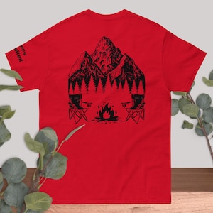May include: Red t-shirt with a black graphic of a mountain range, trees, camping chairs, and a campfire. The text "Campers United" is printed on the left sleeve. The shirt is made of a soft material.