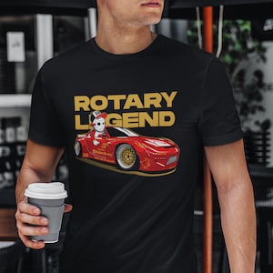 Könnte beinhalten: Ein schwarzes T-Shirt mit einem roten Comic-Auto und einer Figur mit Maske. Der Text "ROTARY LEGEND" ist in goldenen Buchstaben auf dem Shirt.