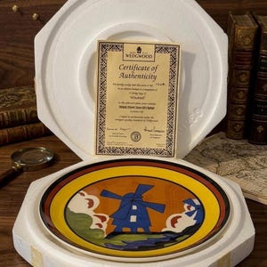 May include: A decorative plate featuring a windmill design in blue, orange, and yellow, presented in a protective foam case. Includes a Wedgwood Certificate of Authenticity. The plate is a collectible item.