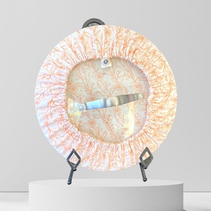 May include: A white and orange floral patterned fabric cover for a pot lid with a metal handle. The cover is on a black stand.