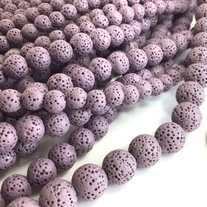 May include: A close-up of a strand of purple lava rock beads. The beads are round and have a rough, textured surface. They are perfect for making jewelry or other crafts.