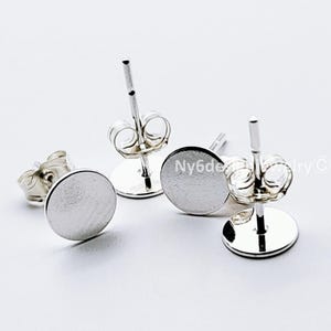 May include: Four silver-colored stud earrings with a flat, circular design. The earrings have a post and butterfly backing. The image is on a white background. The earrings are likely for pierced ears.